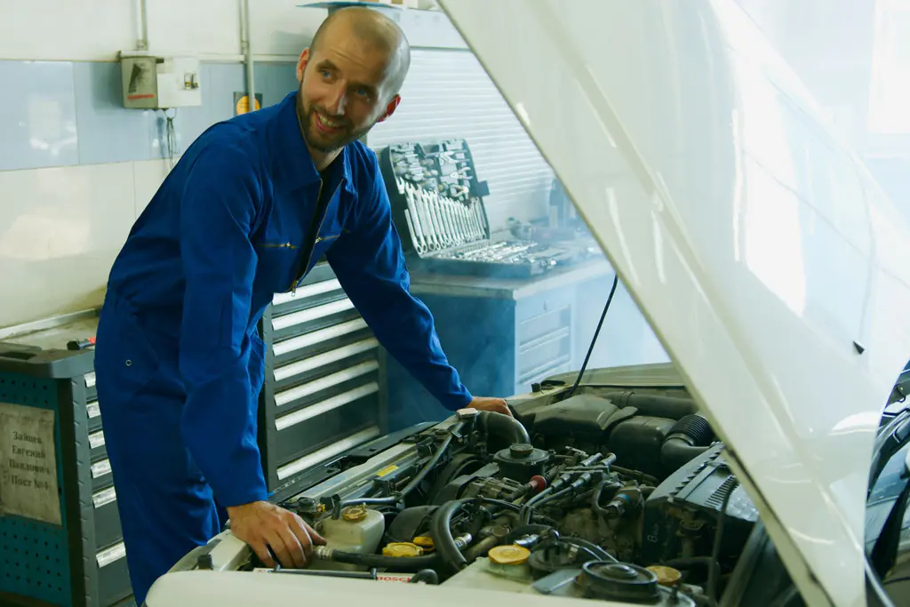 Smiling mechanic working under the hood of a car in a repair shop
